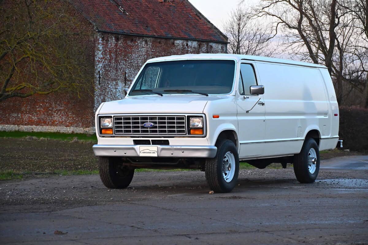 A white vintage cargo van parked outdoors, front view.