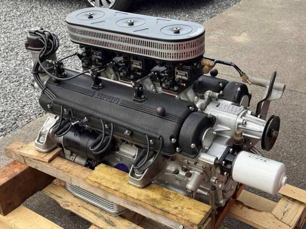 V8 engine with carburetor and intake manifold on wooden pallet.