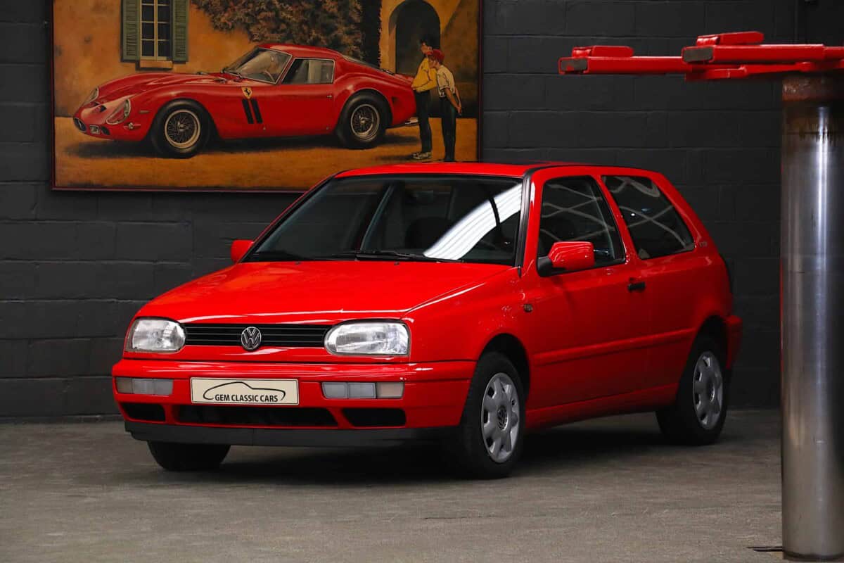 Red Volkswagen Golf hatchback displayed indoors with artwork in background.