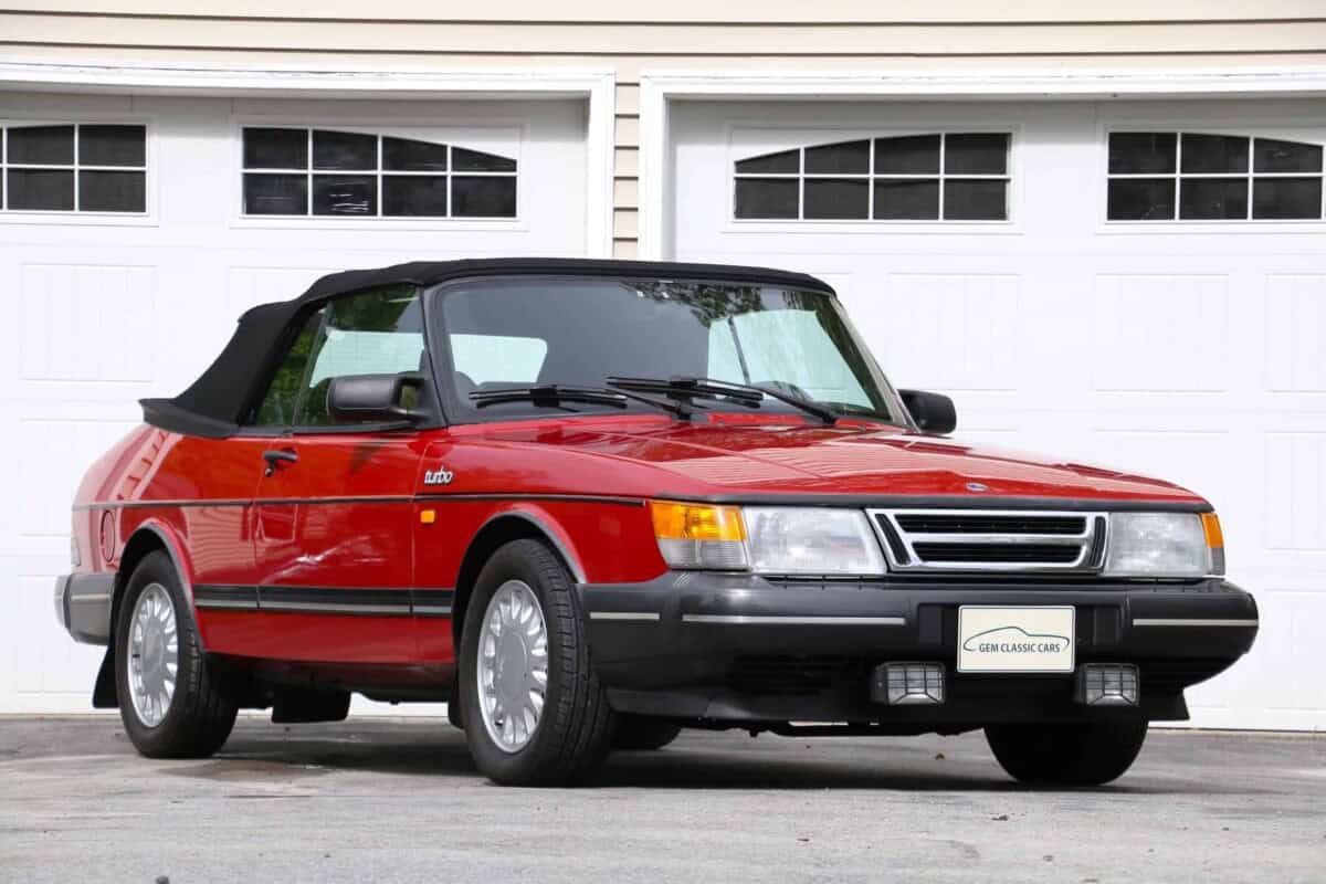Exterior shot of a red Saab convertible parked in front of a garage.