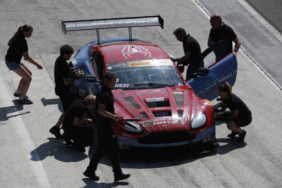 High-angle view of a red and blue race car surrounded by team members in the pit.