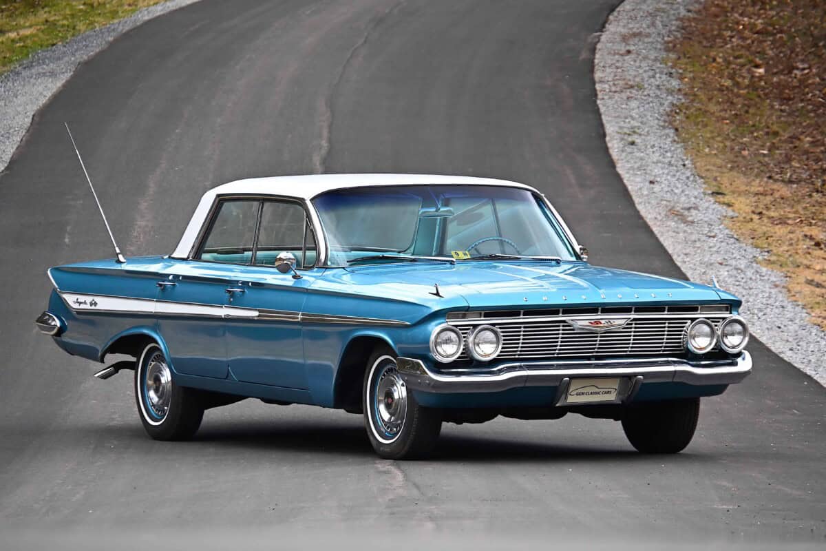 Exterior shot of a vintage 1960s blue classic car driving on a curved road.