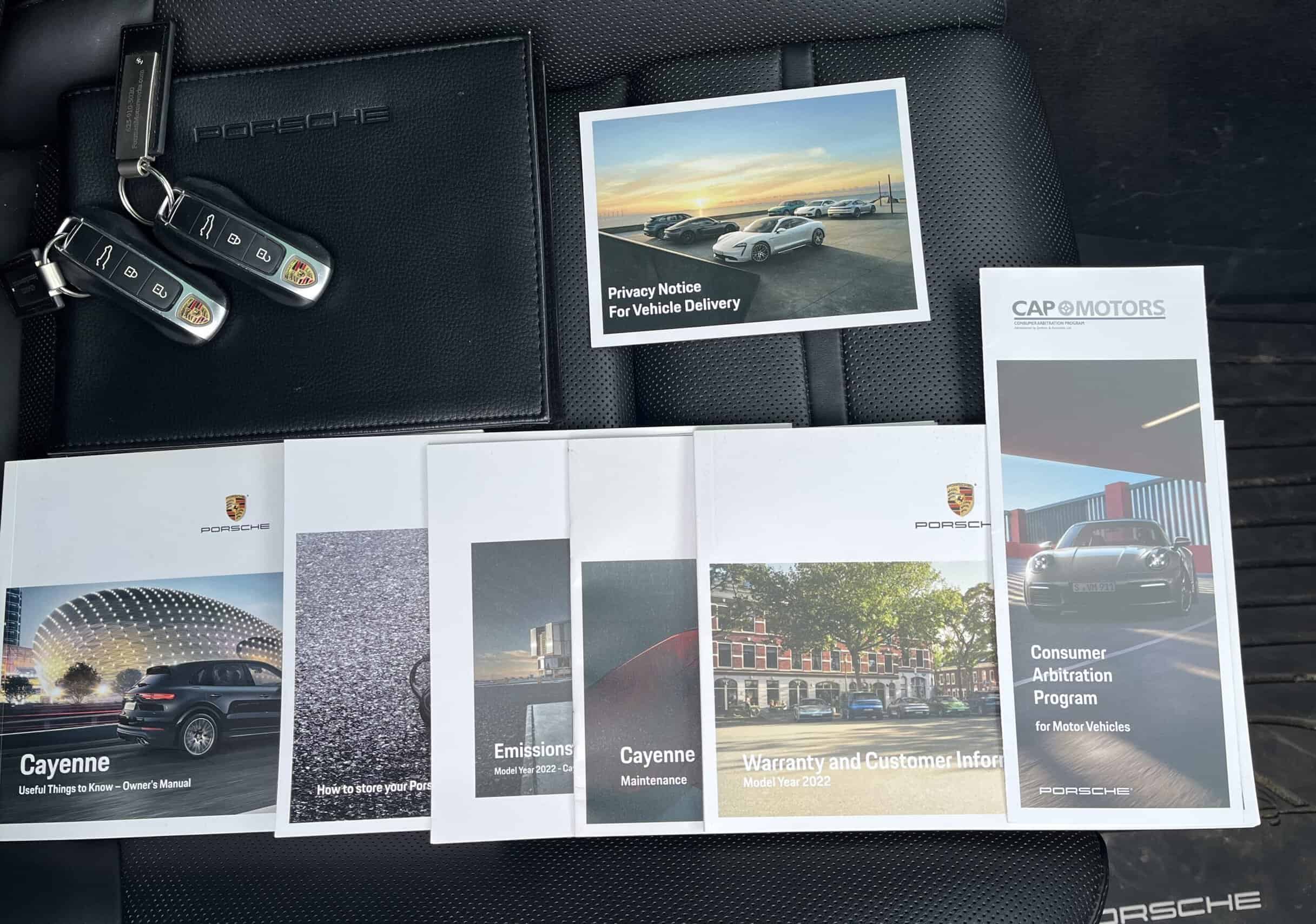 2022 Porsche Cayenne — Collection of car sale documents and keys on black surface.