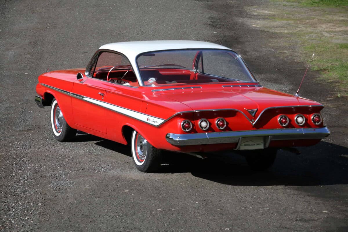 Exterior view of a vintage red and white classic car parked on a gravel road.