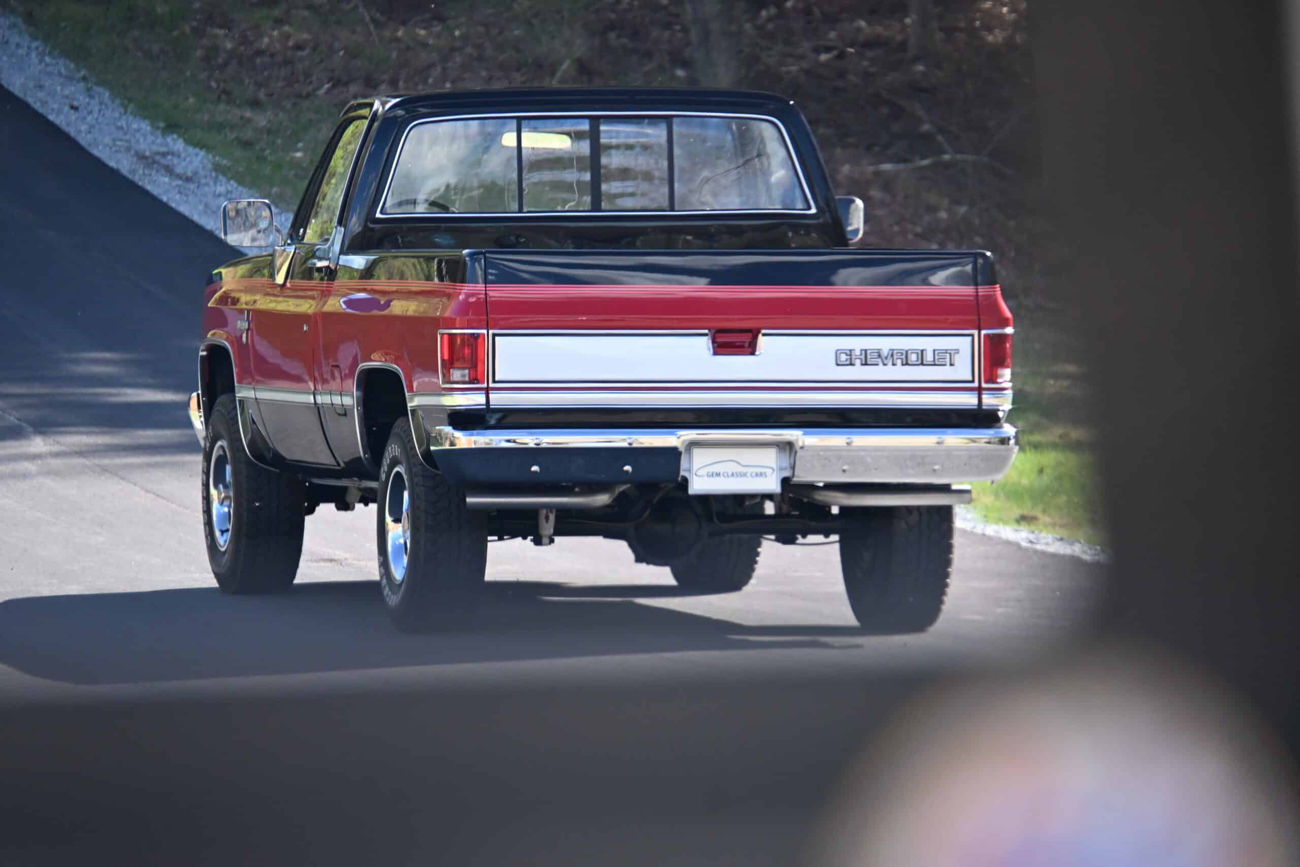 1986 Chevrolet SILVERADO — Red and black classic pickup truck driving on the road.