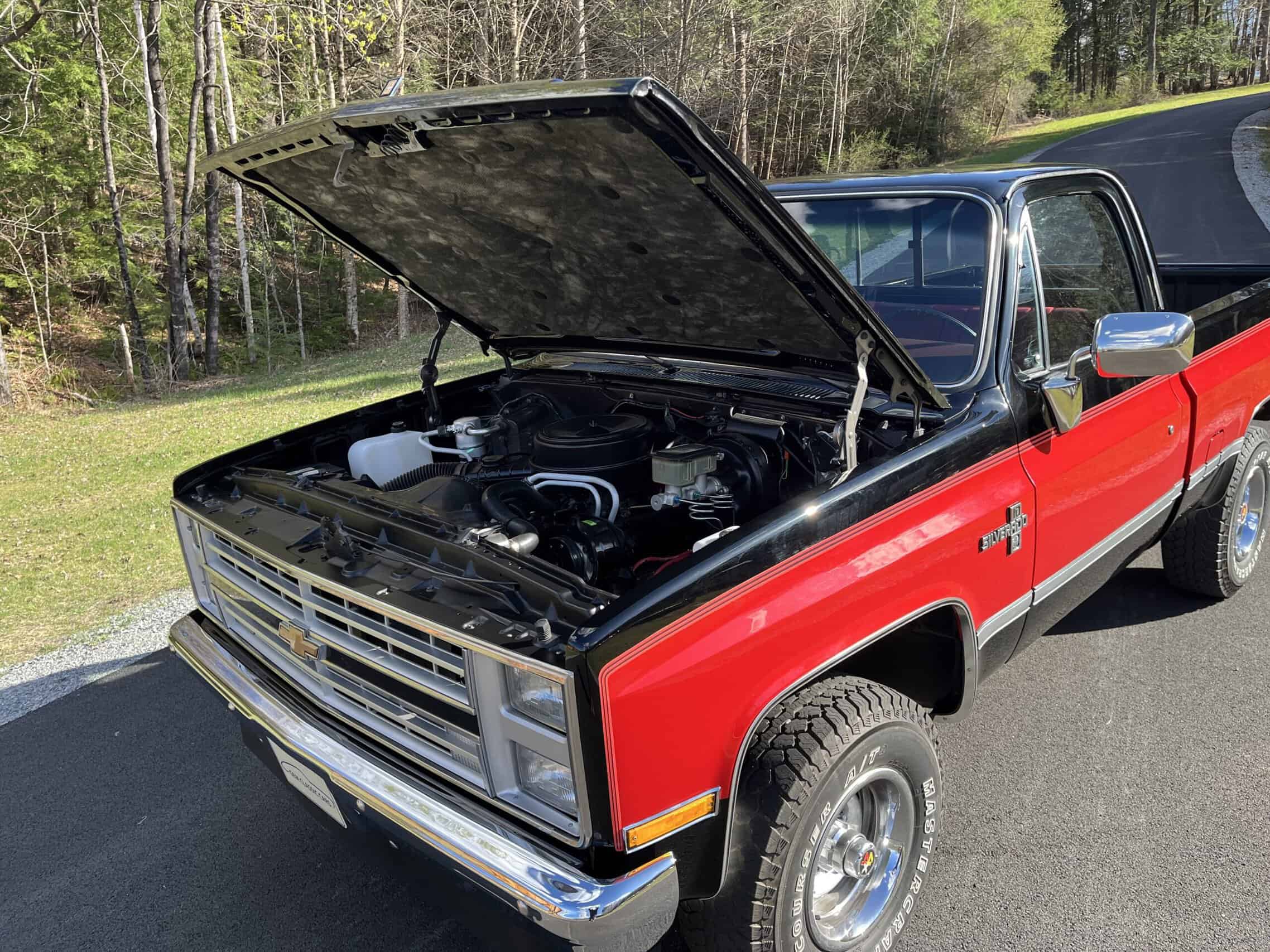 1986 Chevrolet SILVERADO — Red and black classic pickup truck with open hood showing engine.