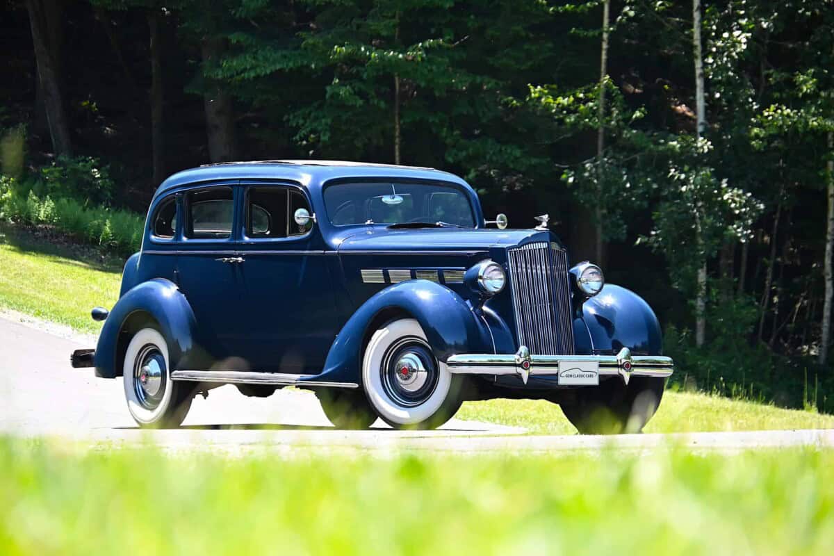 Blue classic car parked outdoors with green trees in background.