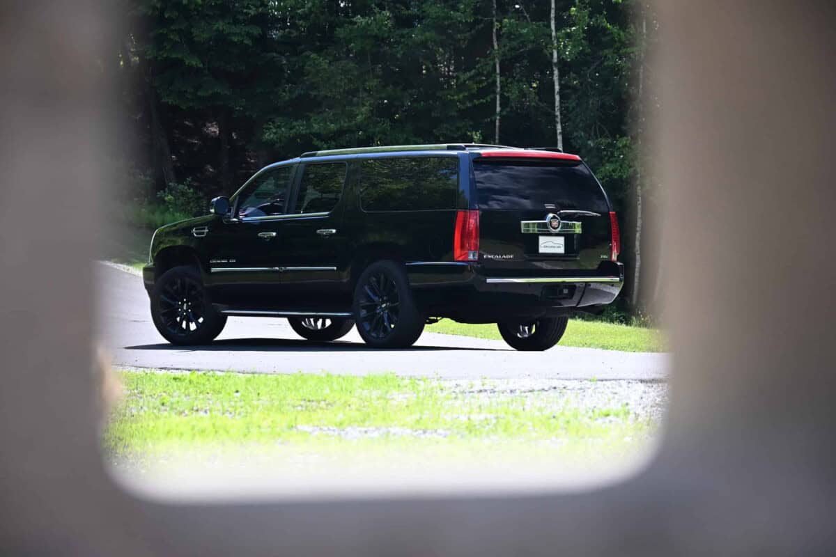 Black classic car SUV seen through a window with trees in background.