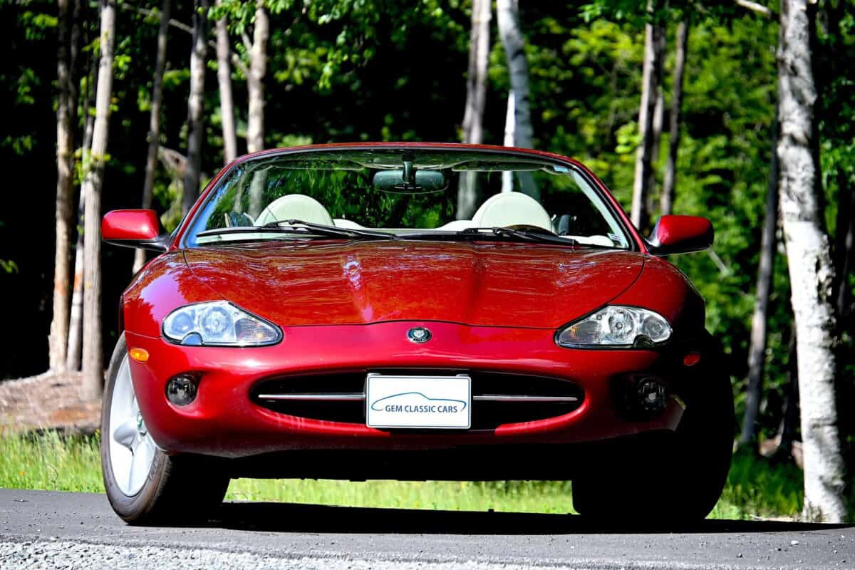 Red classic car convertible with white interior in a forest setting.
