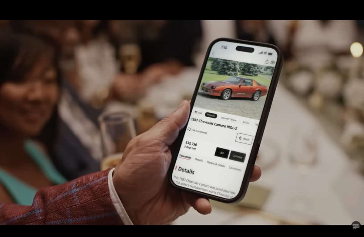 Person browsing classic car listing on smartphone at event.