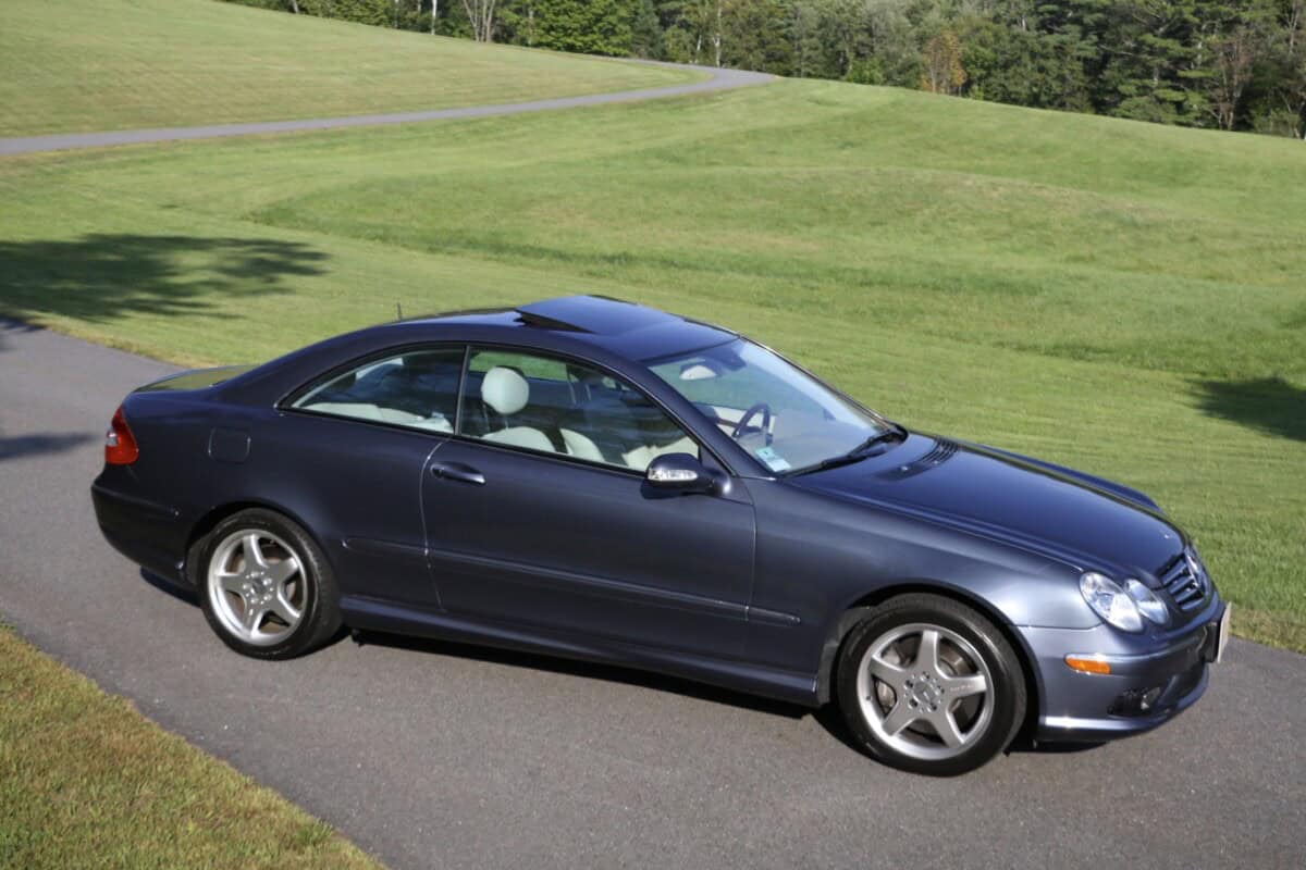 Dark blue classic car coupe parked on driveway with green lawn.