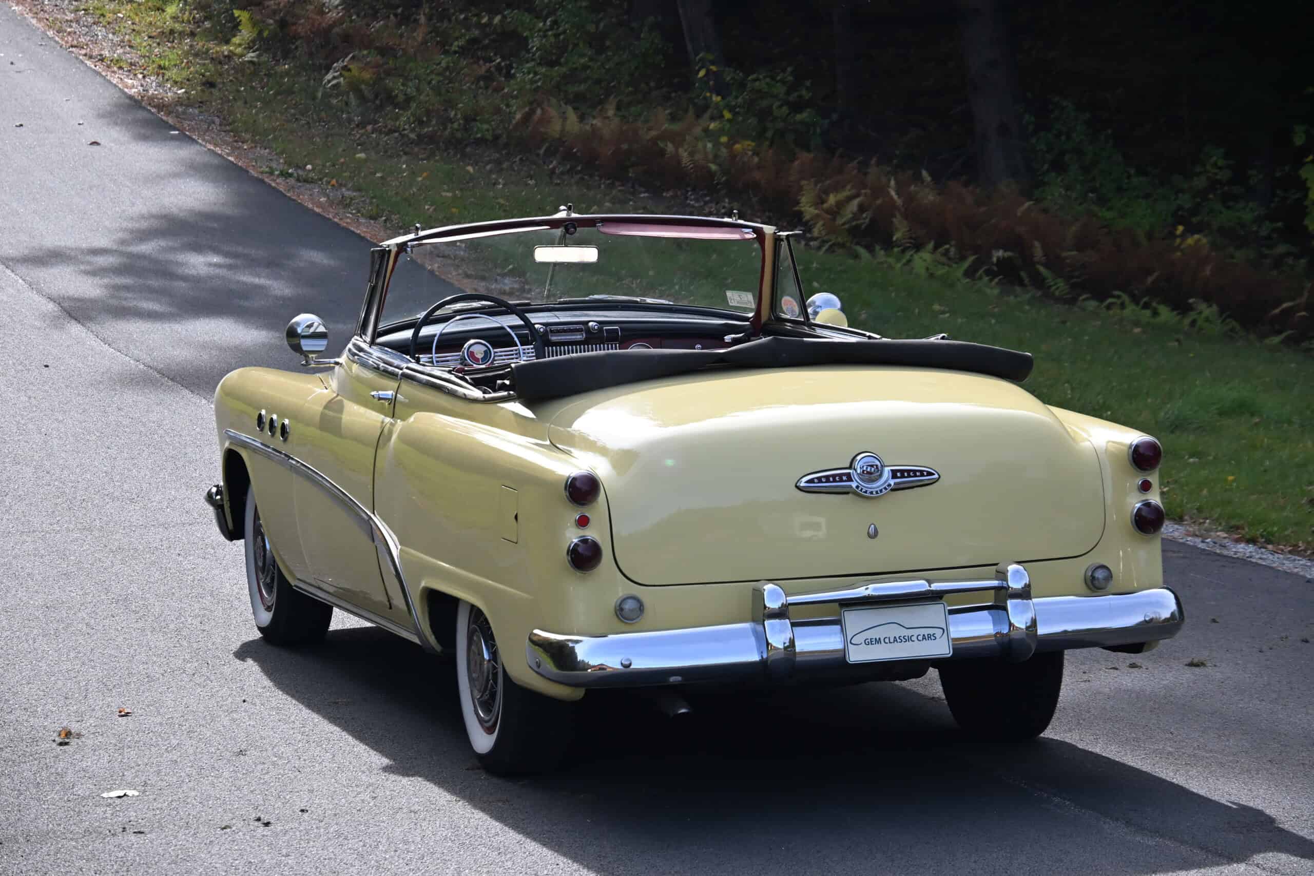 1953 Buick special — Yellow classic car convertible driving on a road with trees.