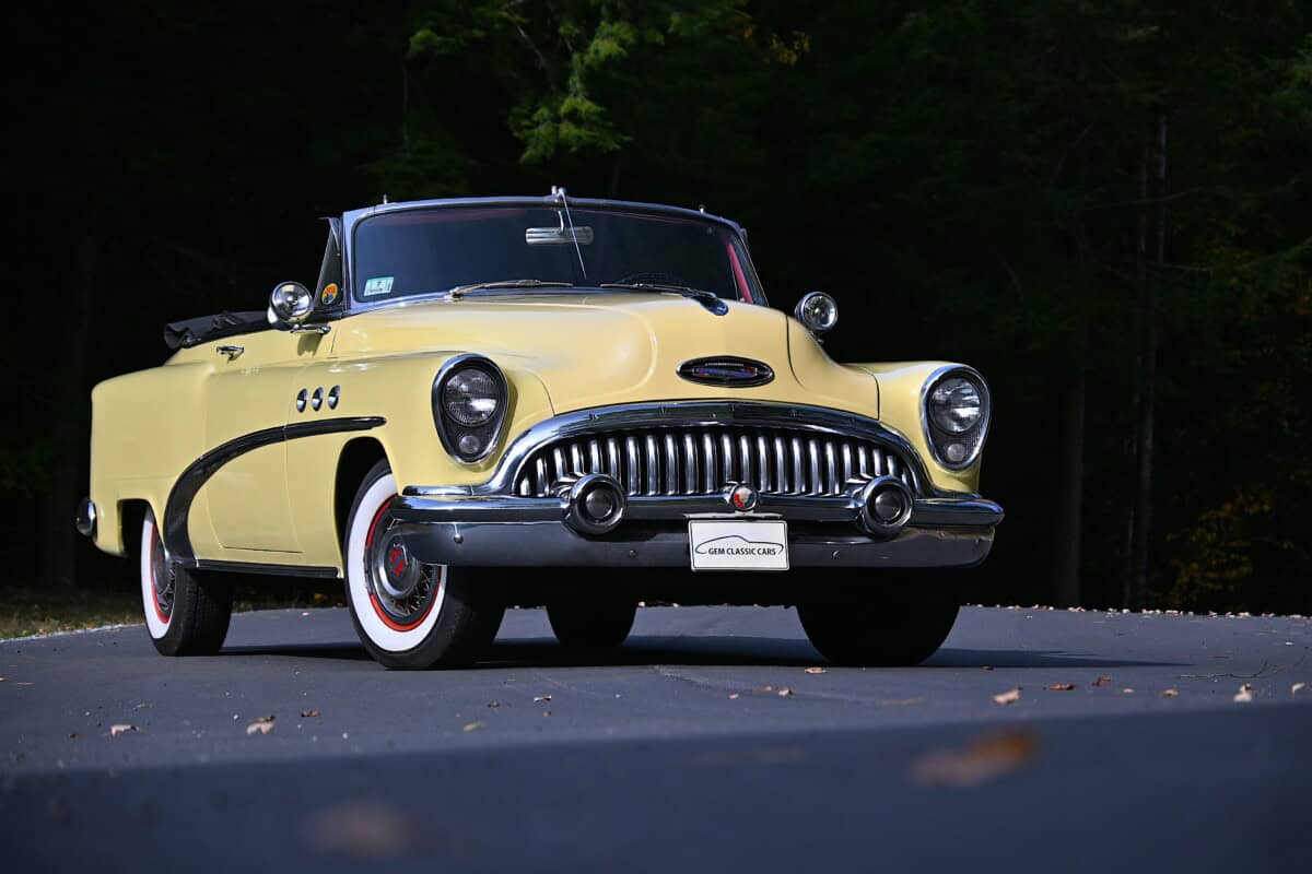 Yellow classic car convertible with chrome grille and whitewall tires.