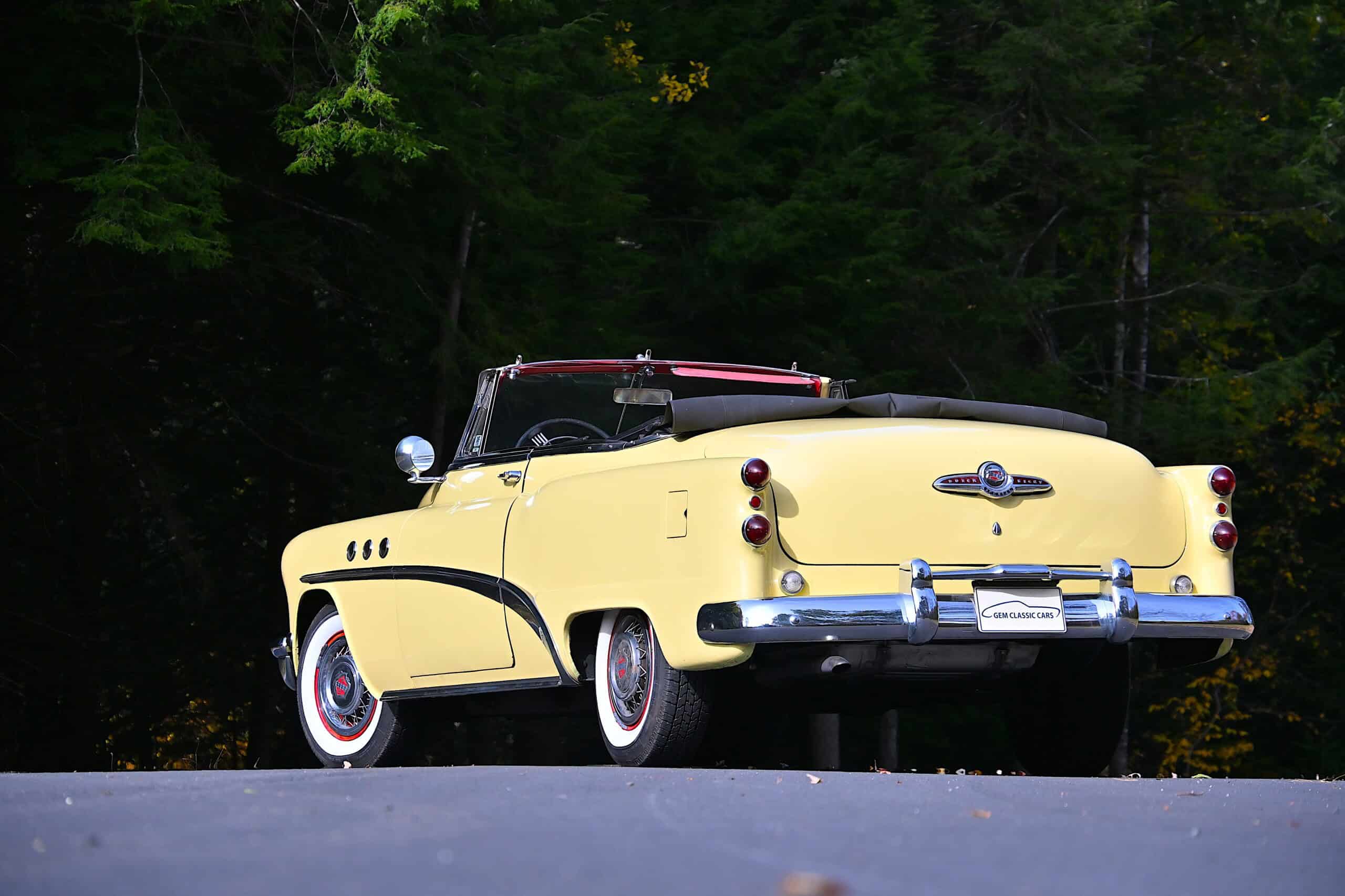 1953 Buick special — Yellow classic car convertible parked on road with green trees in background.