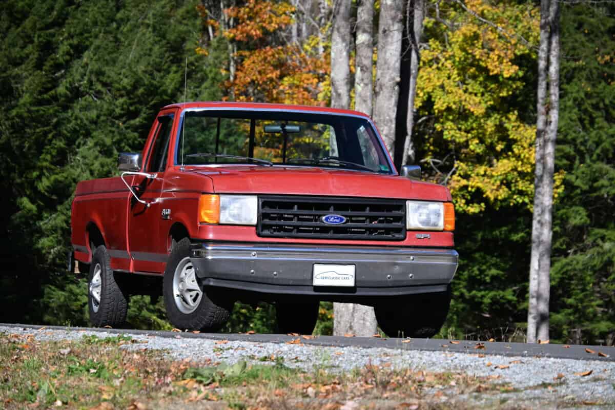 1987 Ford F150 — Classic car exterior on a road with trees in the background, orange body and grn.