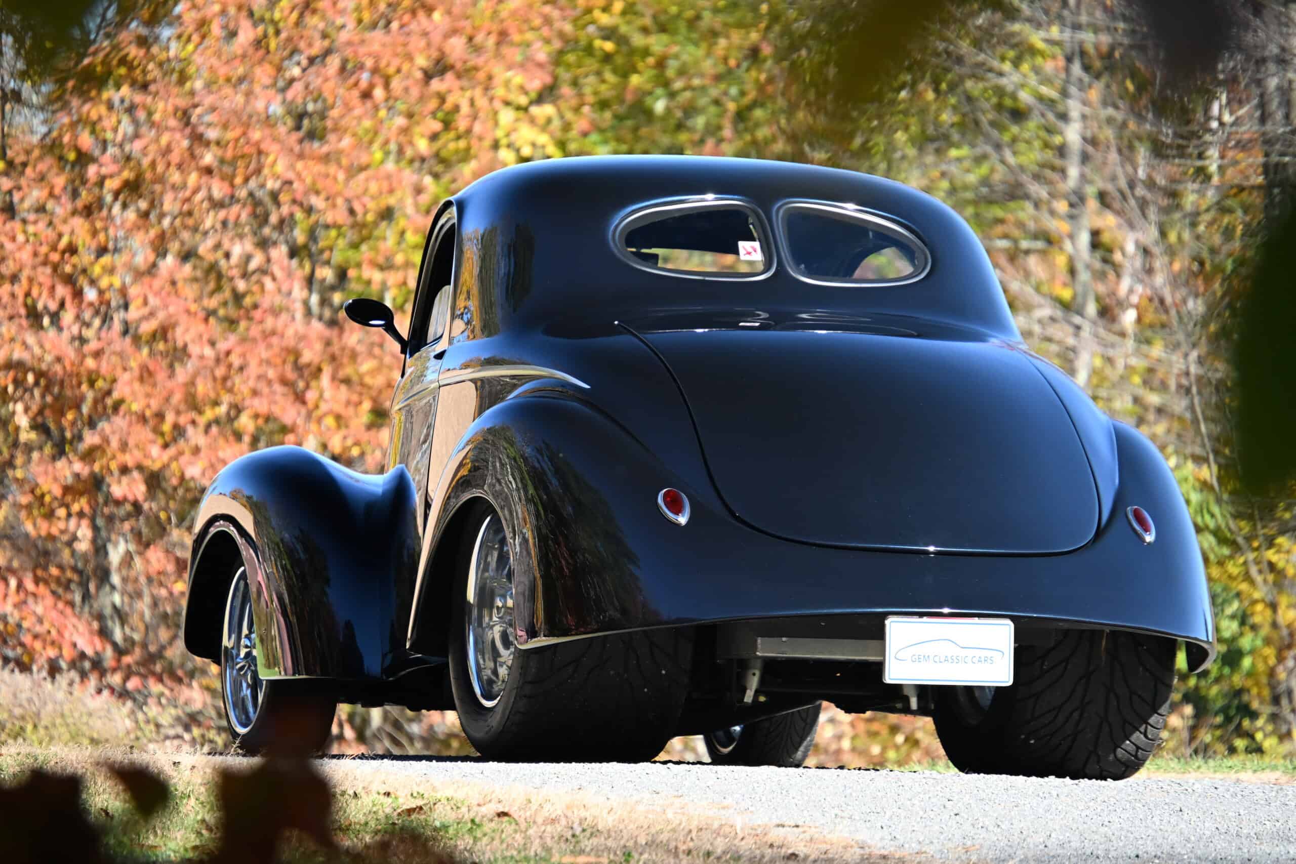 1941 Willys Custom Street Rod — Black classic car with rounded body and rear engine in fall landscape.