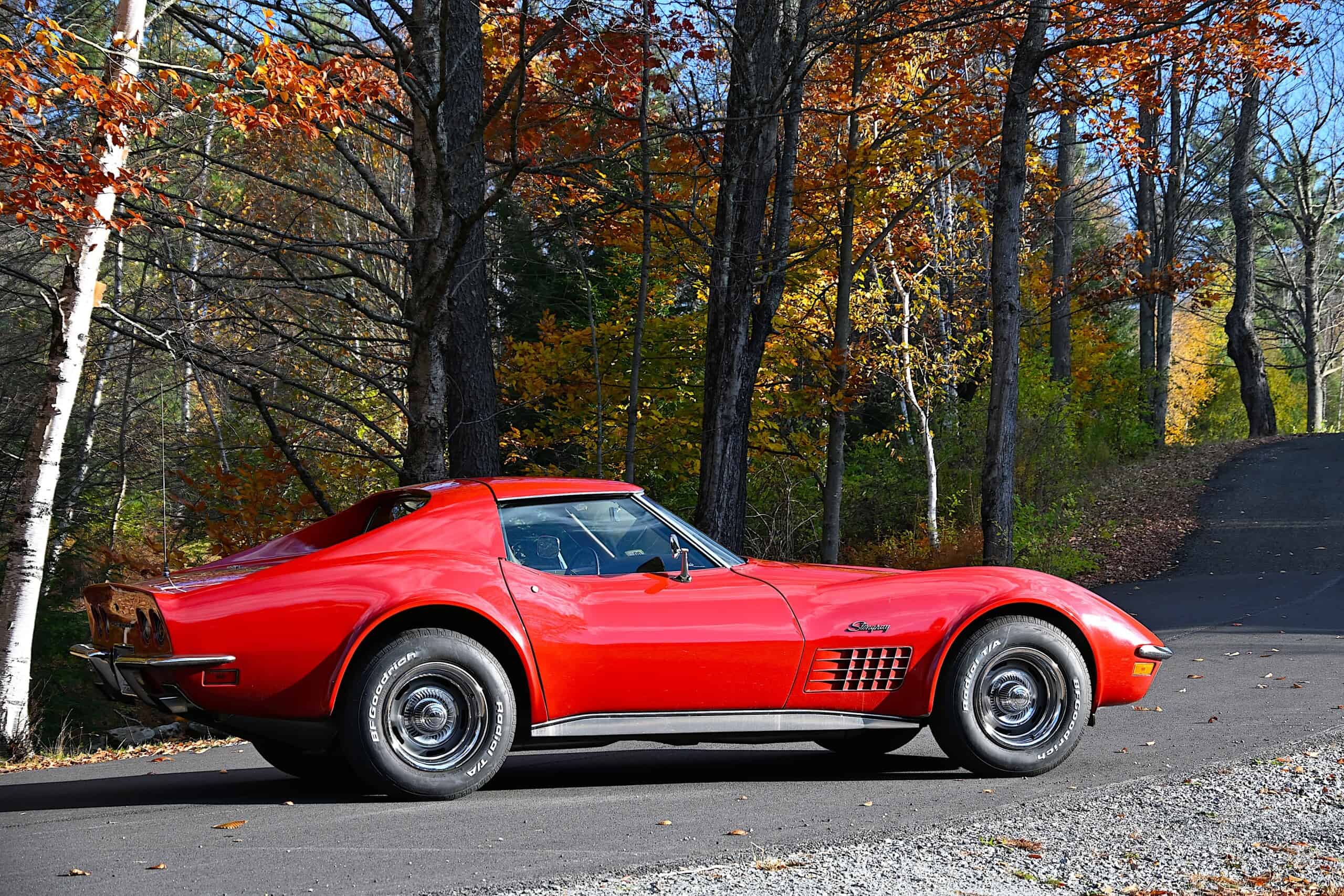 1972 Chevrolet corvette — Red classic car parked on road with autumn trees in background.