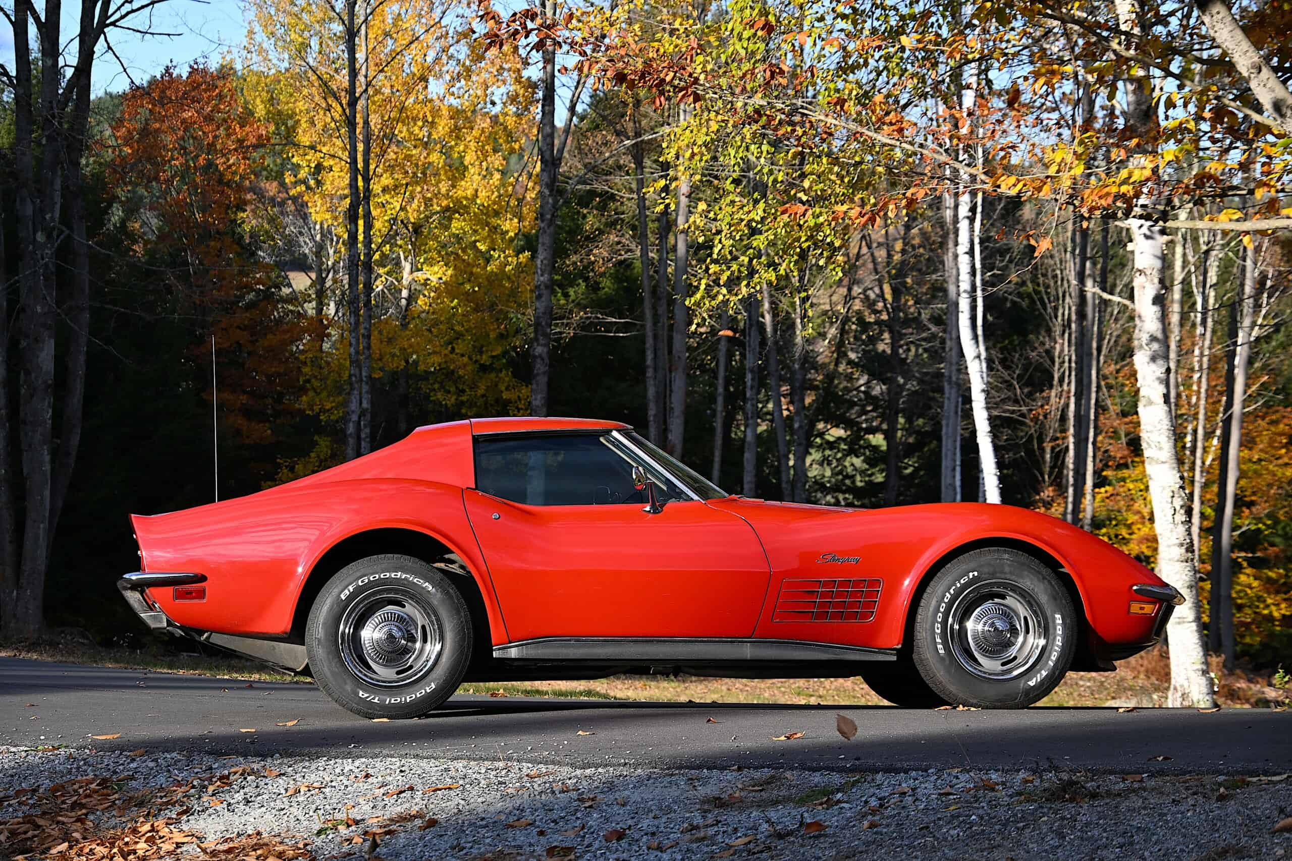 1972 Chevrolet corvette — Red classic car parked on road with autumn trees in background.