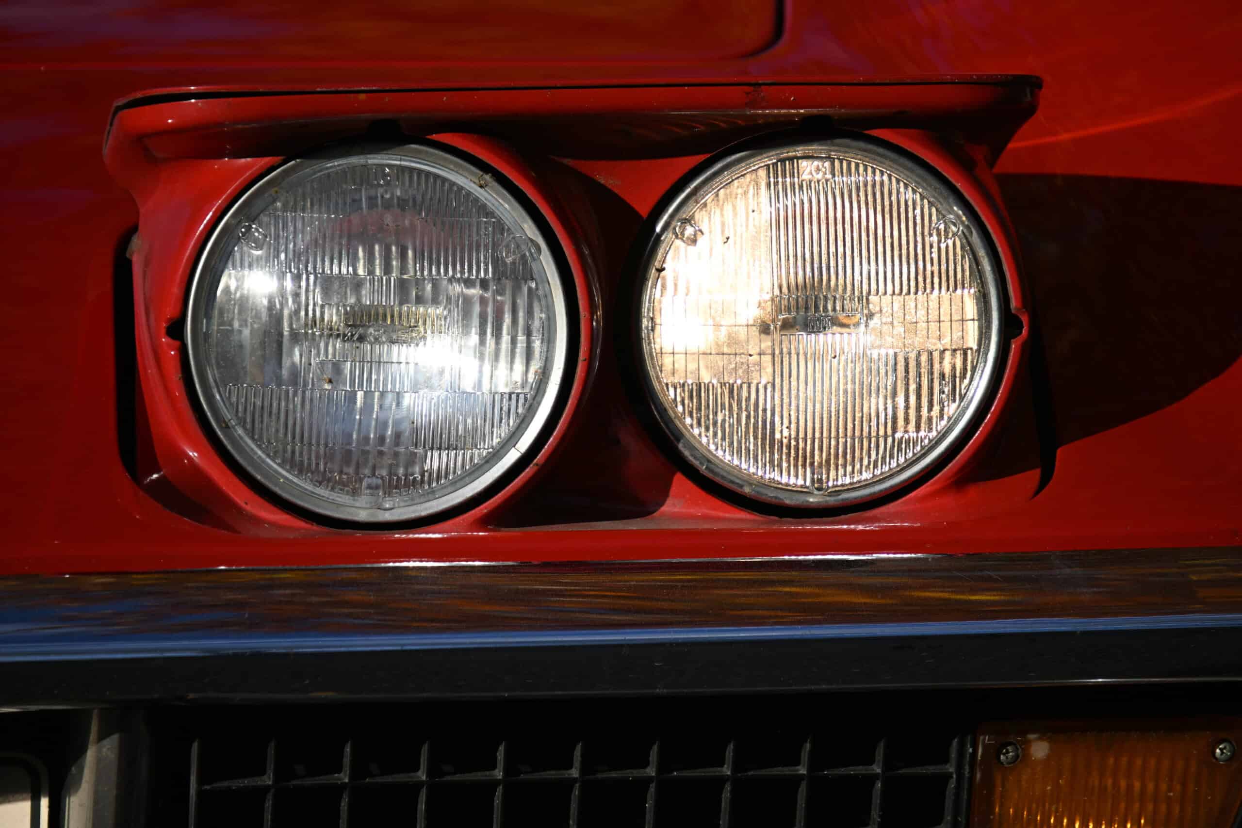 1972 Chevrolet corvette — Close-up of round classic car headlights on red exterior.