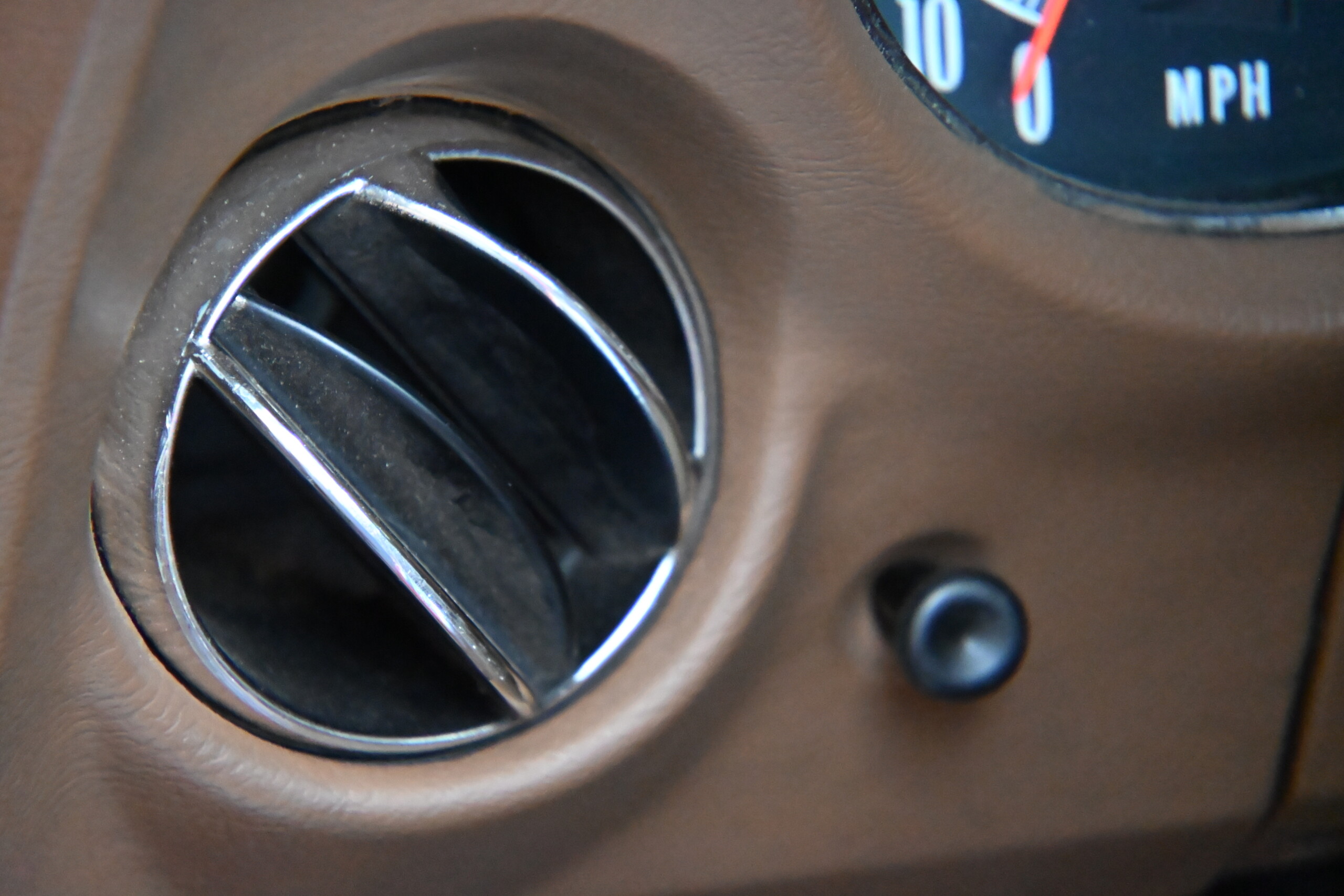 1972 Chevrolet corvette — Close-up of round air vent in classic car interior with brown dashboard.